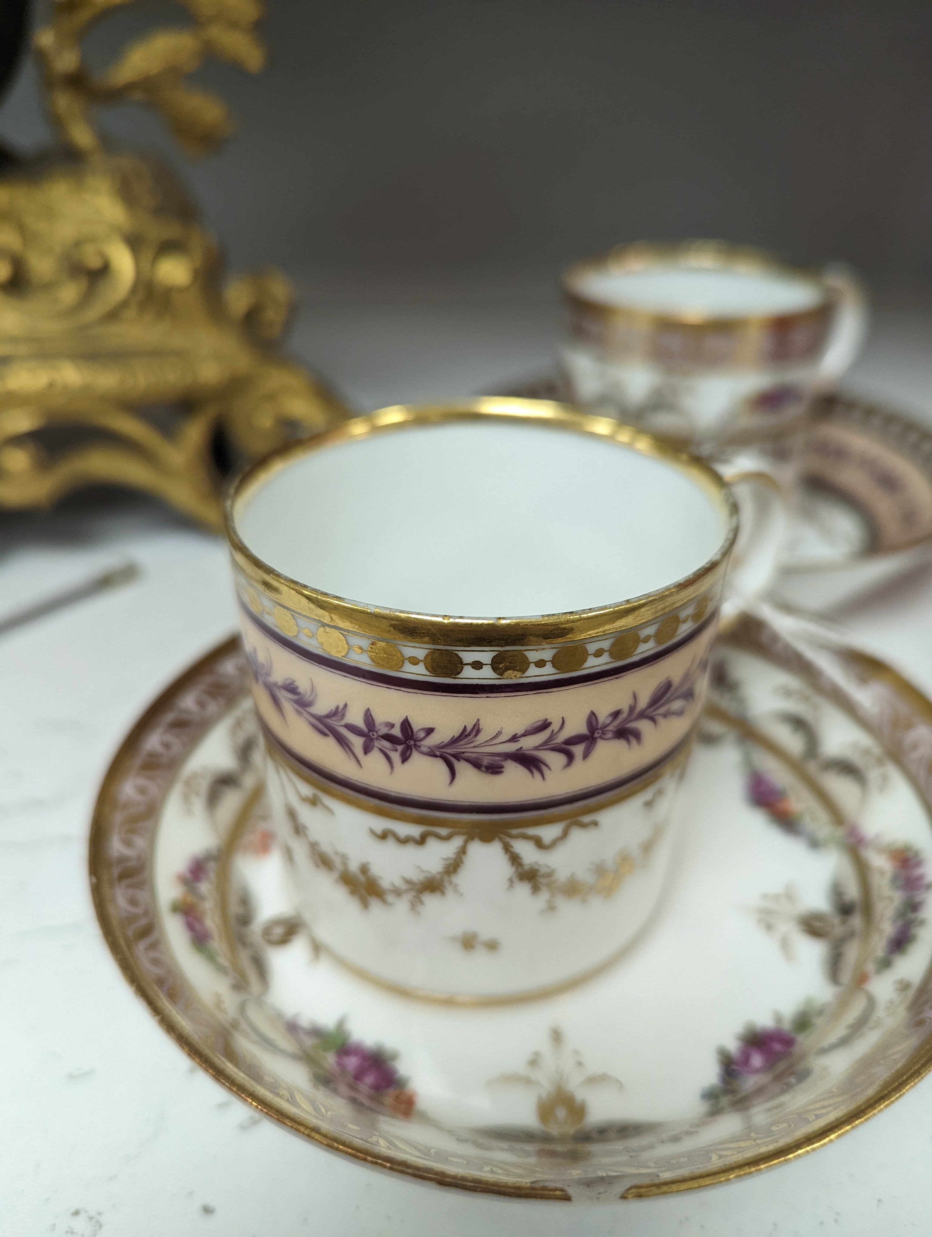 A Duc d'Angouleme coffee can and saucer painted with a puce chain of leaves on a salmon coloured ground and another painted with a flower chain, black feather and a gilt line, latter with stencilled red mark 'Manuf de M